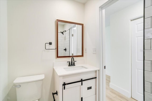 bathroom featuring hardwood / wood-style floors, vanity, toilet, and tiled shower