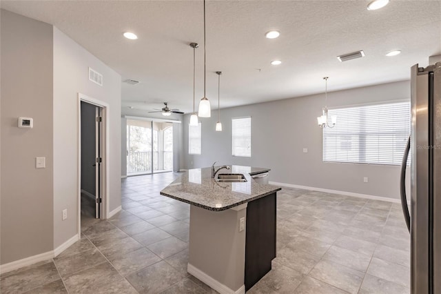 kitchen with stainless steel refrigerator, hanging light fixtures, dark stone counters, and sink