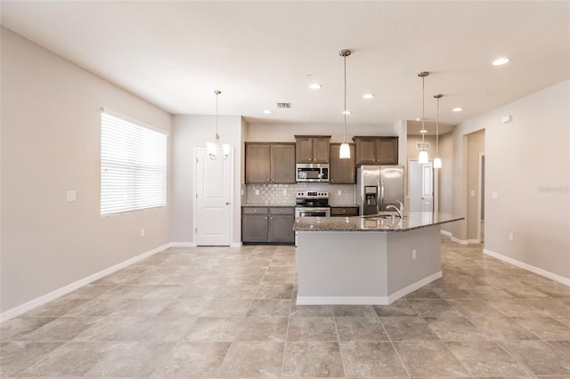 kitchen featuring dark stone countertops, pendant lighting, an island with sink, and stainless steel appliances