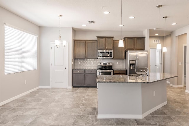 kitchen featuring decorative light fixtures, dark stone countertops, stainless steel appliances, and an island with sink