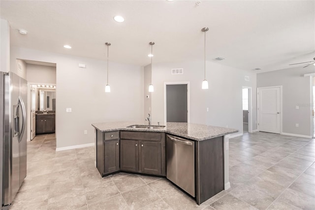 kitchen with dark brown cabinets, light stone countertops, stainless steel appliances, and an island with sink