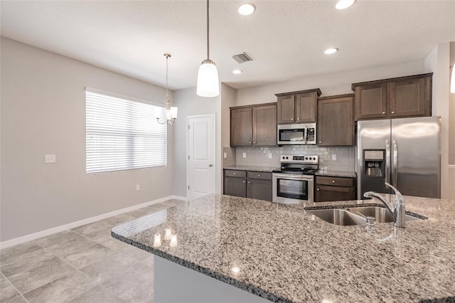 kitchen with appliances with stainless steel finishes, light stone counters, dark brown cabinetry, sink, and hanging light fixtures