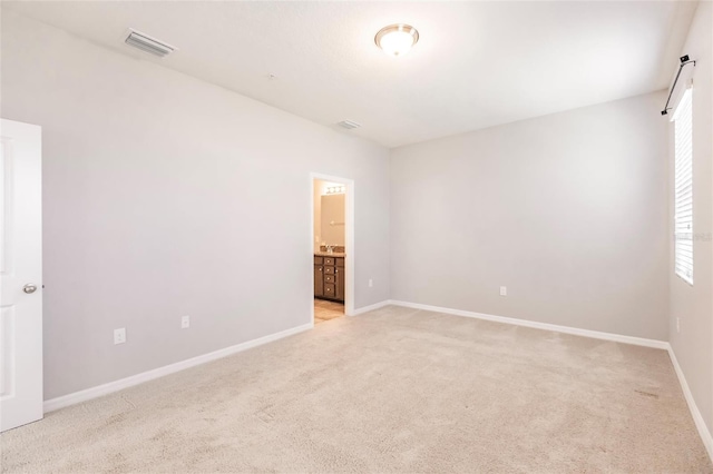 unfurnished bedroom featuring light carpet and ensuite bath