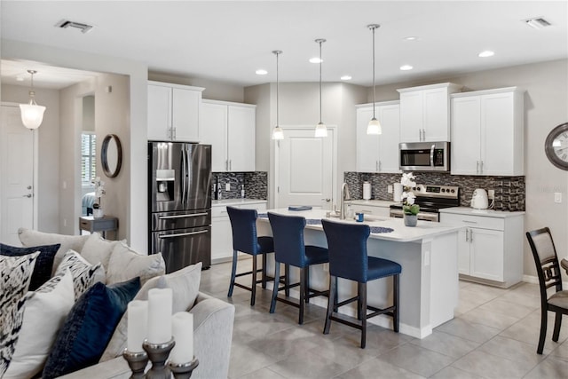 kitchen with white cabinetry, hanging light fixtures, stainless steel appliances, and a center island with sink