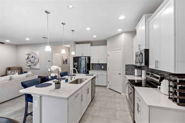 kitchen featuring stainless steel appliances, a kitchen island with sink, sink, white cabinetry, and hanging light fixtures