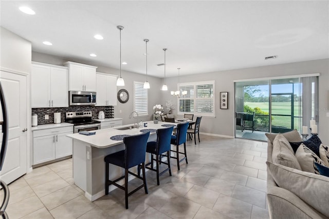 kitchen with a breakfast bar, a kitchen island with sink, sink, appliances with stainless steel finishes, and decorative light fixtures