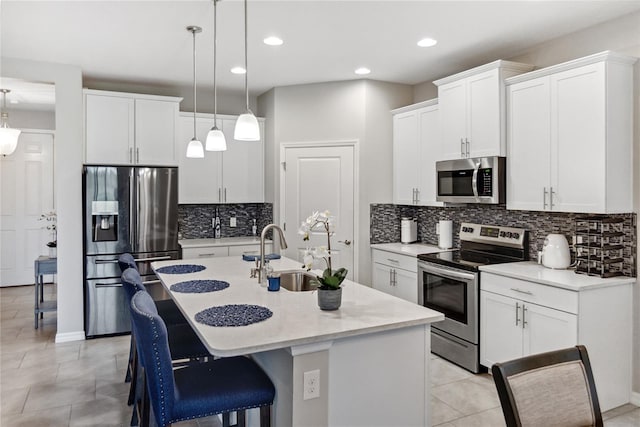 kitchen featuring appliances with stainless steel finishes, sink, white cabinetry, hanging light fixtures, and an island with sink