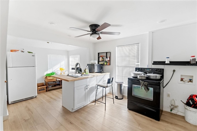 kitchen with light hardwood / wood-style floors, sink, white cabinets, white fridge, and black / electric stove