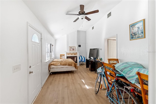 bedroom with ceiling fan, light wood-type flooring, lofted ceiling, and a fireplace