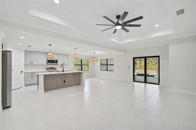 kitchen with appliances with stainless steel finishes, a center island with sink, a raised ceiling, and a healthy amount of sunlight