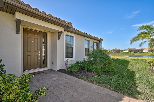 view of exterior entry featuring a water view and a lawn