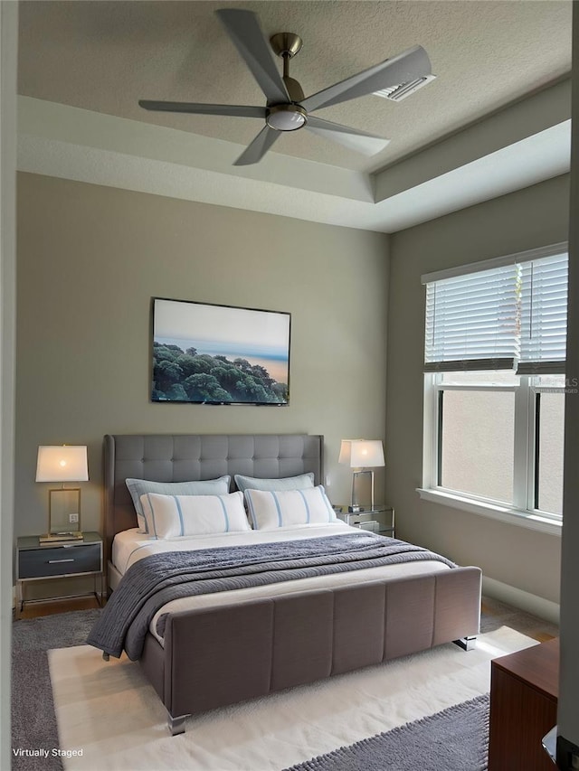 bedroom featuring ceiling fan, a raised ceiling, carpet floors, and a textured ceiling