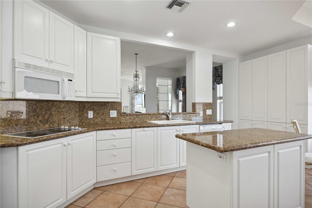 kitchen with kitchen peninsula, sink, dark stone counters, and white appliances