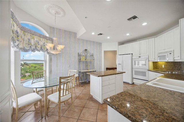 kitchen with white appliances, pendant lighting, light tile patterned floors, white cabinets, and a center island