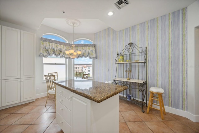 kitchen featuring white cabinets, light tile patterned floors, a center island, and dark stone counters