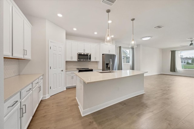 kitchen with tasteful backsplash, stainless steel appliances, decorative light fixtures, white cabinets, and light hardwood / wood-style floors