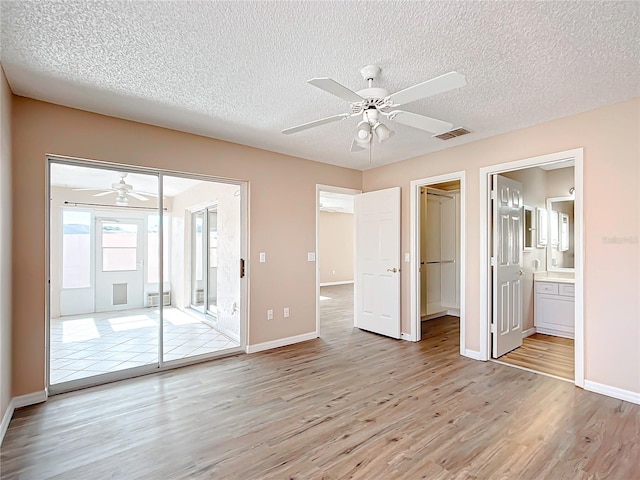 unfurnished bedroom with ensuite bath, a textured ceiling, ceiling fan, light hardwood / wood-style flooring, and a closet