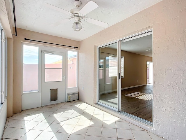 interior space featuring a wall mounted air conditioner, light tile patterned floors, a textured ceiling, and ceiling fan