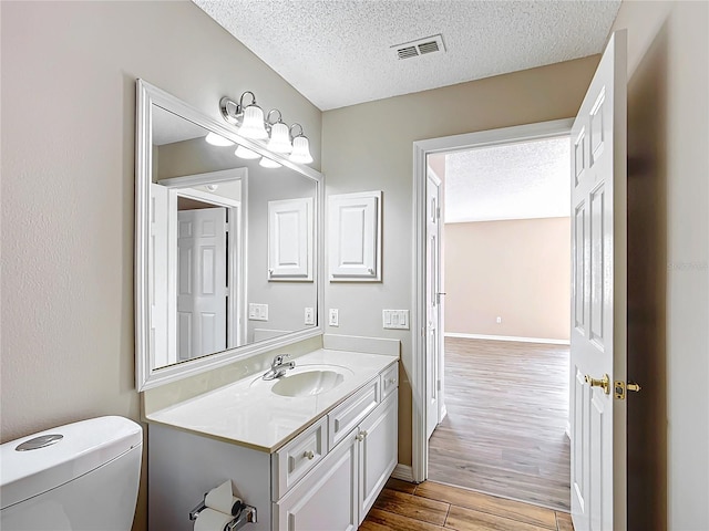 bathroom featuring wood-type flooring, toilet, vanity, and a textured ceiling