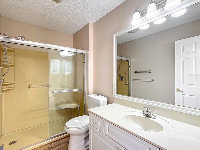 bathroom featuring vanity, toilet, a shower with shower door, and a textured ceiling