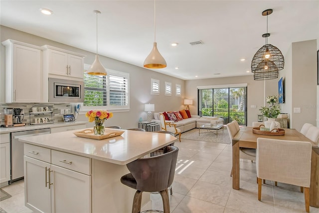 kitchen featuring white cabinetry, hanging light fixtures, stainless steel appliances, backsplash, and a kitchen island