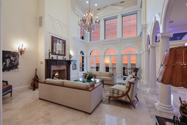 living room with an inviting chandelier, a high end fireplace, decorative columns, a towering ceiling, and ornamental molding