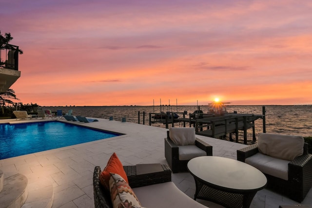 pool at dusk with an outdoor hangout area, a water view, and a patio area