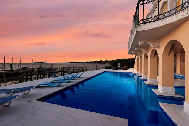 pool at dusk featuring a patio area and a water view