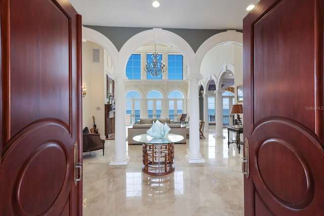 entrance foyer featuring a healthy amount of sunlight, a water view, ornate columns, and an inviting chandelier