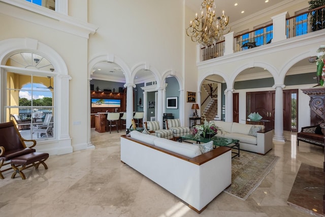 living room with a chandelier, a high ceiling, ornate columns, and ornamental molding