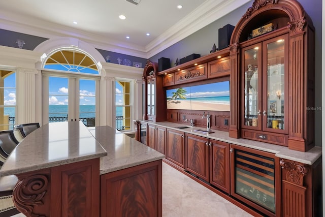 bar with light stone countertops, french doors, beverage cooler, crown molding, and a water view