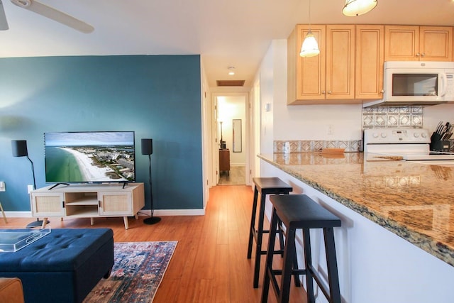 kitchen with white appliances, light wood-type flooring, light brown cabinetry, decorative light fixtures, and light stone counters