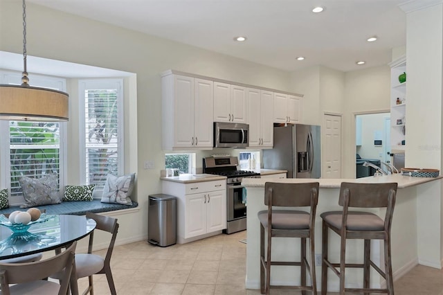 kitchen with kitchen peninsula, stainless steel appliances, white cabinets, hanging light fixtures, and light tile patterned flooring