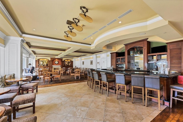 kitchen with a kitchen bar, light tile patterned floors, coffered ceiling, and ornamental molding