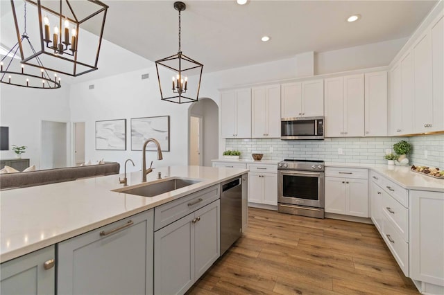 kitchen with stainless steel appliances, sink, light hardwood / wood-style flooring, white cabinetry, and hanging light fixtures