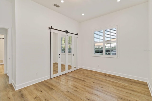 unfurnished bedroom featuring a barn door, light hardwood / wood-style floors, and a closet