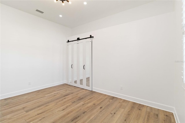 unfurnished room with a barn door and light hardwood / wood-style floors