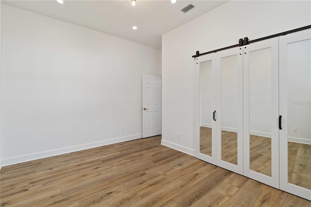 unfurnished bedroom with a barn door and light hardwood / wood-style floors