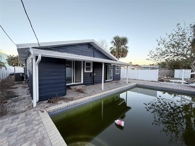 back house at dusk featuring a fenced in pool and central AC unit