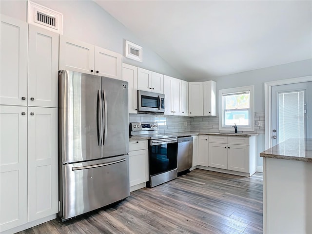 kitchen with white cabinets, dark hardwood / wood-style floors, lofted ceiling, and appliances with stainless steel finishes