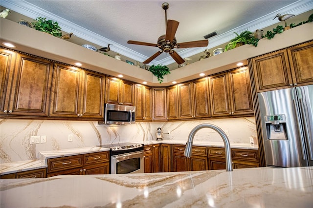 kitchen featuring tasteful backsplash, light stone counters, ornamental molding, stainless steel appliances, and ceiling fan