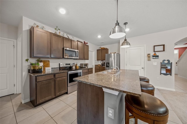 kitchen featuring sink, light tile patterned floors, appliances with stainless steel finishes, decorative light fixtures, and a breakfast bar area