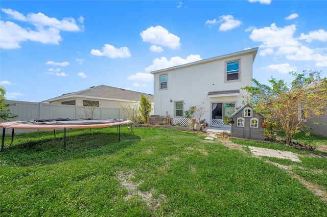 back of property with a yard, a storage unit, and a trampoline