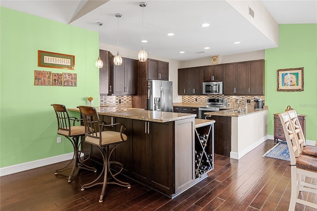 kitchen featuring a breakfast bar, kitchen peninsula, pendant lighting, dark brown cabinets, and appliances with stainless steel finishes