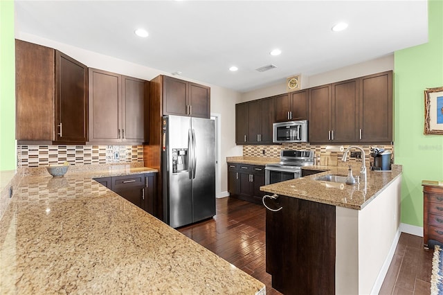 kitchen featuring kitchen peninsula, appliances with stainless steel finishes, backsplash, light stone countertops, and sink