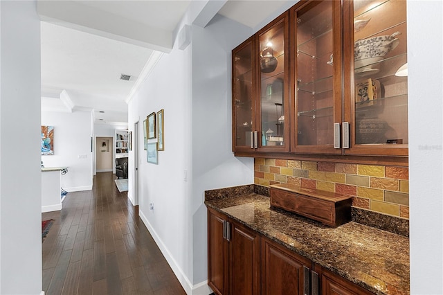 bar with crown molding, dark stone countertops, backsplash, and dark wood-type flooring