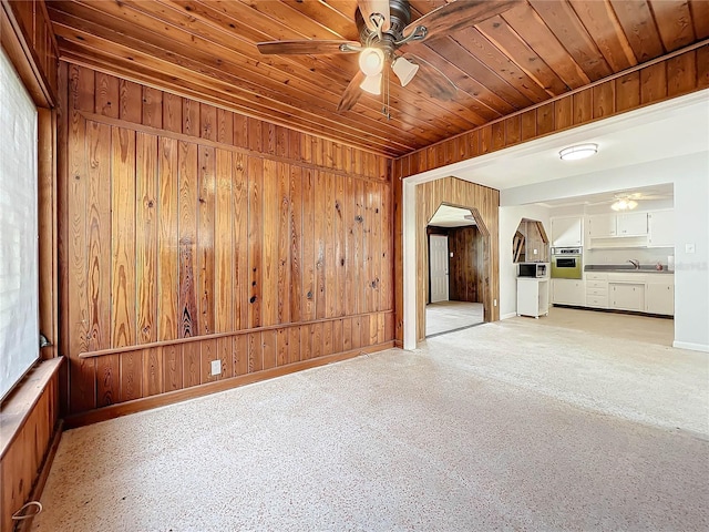 empty room featuring wood walls, ceiling fan, wooden ceiling, and light carpet