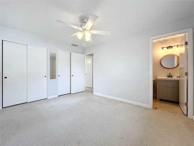 unfurnished bedroom featuring two closets, ensuite bath, ceiling fan, and sink