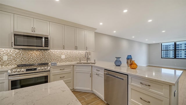 kitchen featuring light stone countertops, light wood-type flooring, stainless steel appliances, and sink