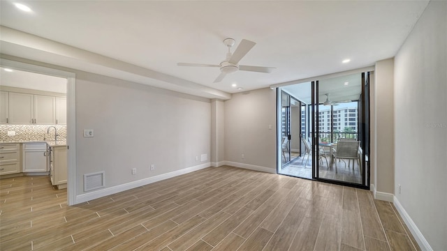 spare room featuring light wood-type flooring, expansive windows, ceiling fan, and sink